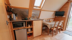 A compact kitchen with a microwave, sink, and wooden cabinets. There's a dining table with chairs and a TV mounted on the wall. - Rustic Coastal Cabin with Wood Fired Hot Tub (Cockburnspath)