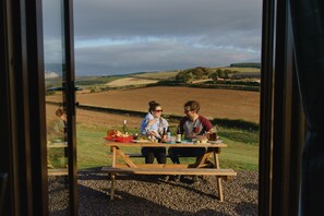 Deux personnes sont assises à une table de pique-nique en bois, devant un paysage rural.