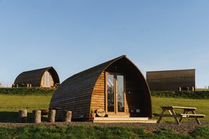 Une cabane en bois dotée d’une grande porte-fenêtre coulissante, d’une table de pique-nique et d’une petite plante en pot.