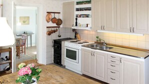 Une cuisine avec des meubles blancs, une table en bois, une cuisinière et des casseroles suspendues.