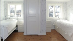 Une chambre avec deux lits, une porte blanche et des fenêtres ornées de papier peint à motifs floraux.