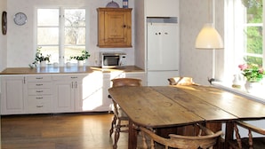 Une cuisine avec des meubles blancs, une table en bois et une fenêtre ornée de plantes.