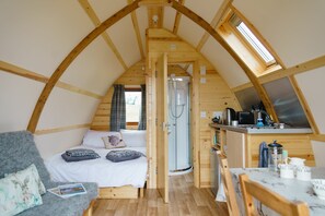 Un interior acogedor de madera con cama en altillo, kitchenette pequeña y ducha.