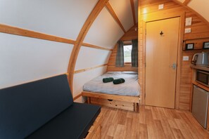 Una habitación compacta con paneles de madera, una cama alta, un pequeño kitchenette y vistas a través de una ventana con cortinas.