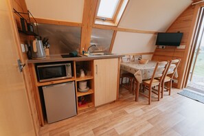 Una cocina compacta con microondas, pileta y muebles de madera. Hay una mesa con sillas y un televisor montado en la pared.