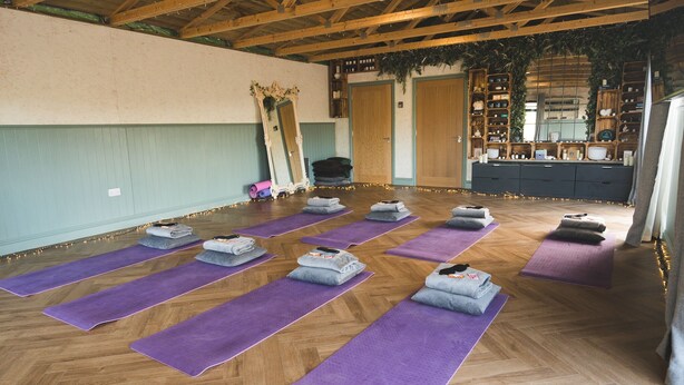 Ein Yoga-Studio mit Holzbalken, violetten Yoga-Matten und einem Spiegel an der Wand.