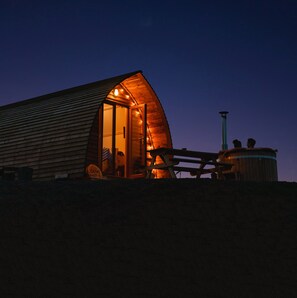 Una cabaña de madera con puerta de vidrio, mesa de picnic y jacuzzi.