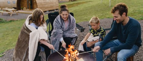 Un groupe de personnes fait griller des guimauves autour d’un feu de camp.