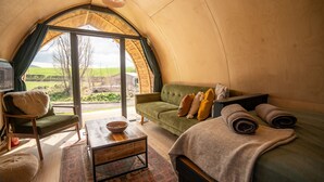 Una habitación acogedora y bien iluminada con un sofá verde, una mesa de centro de madera y un gran ventanal con vistas al campo.