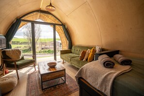 Una habitación acogedora y bien iluminada con un sofá verde, una mesa de centro de madera y un gran ventanal con vistas al campo.