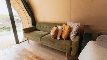 A green sofa with patterned cushions in a room with wooden flooring and a large window.
