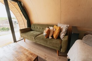 A green sofa with patterned cushions in a room with wooden flooring and a large window.