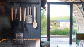 Una cocina con utensilios colgantes y vista a una casa a través de una puerta de cristal.