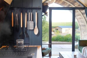 Una cocina con utensilios colgantes y vista a una casa a través de una puerta de cristal.
