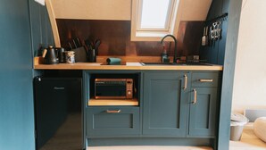 Una cocina compacta con microondas integrado, un lavamanos y un refrigerador pequeño.