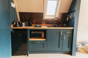 Una cocina compacta con microondas integrado, un lavamanos y un refrigerador pequeño.