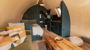 Una stanza accogliente e compatta con un letto, un tavolo in legno e un angolo cottura.