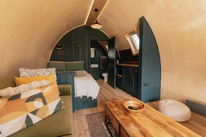Een gezellige, compacte kamer met een bed, een houten tafel en een kleine keukenhoek.