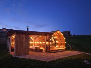Une charmante cabane en bois avec un toit incurvé, une cheminée et un coin salon agrémenté de coussins.