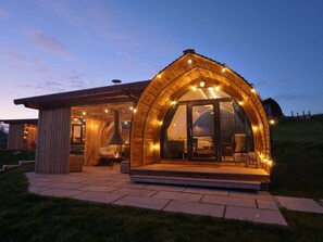 Una cabaña acogedora de madera con un amplio acceso por una puerta de cristal, chimenea y zona de estar con mesa y sillas.