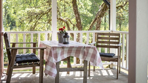 A covered porch with a table and chairs, a potted plant, and a lantern. - Måbäcken by Interhome (Torestorp)