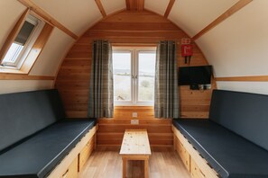 A cozy cabin interior with a wooden bench seating area, a small table, and a window with curtains. - Coastal Family Cabin with Wood Fired Hot Tub (Cockburnspath)