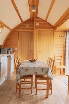 A wooden dining area with a table set for four, a wooden chair, and a wooden cabinet. - Coastal Family Cabin with Wood Fired Hot Tub (Cockburnspath)