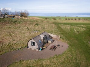 Ein kleines, eingeschossiges Haus mit gewölbtem Dach, einer Terrasse mit Tisch und Bänken und Blick auf das Meer.