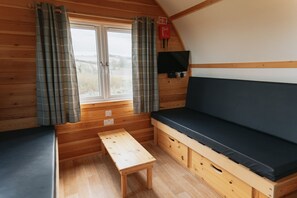 A cabin with a wooden interior, a bench, a sofa, a window with curtains, and a fire extinguisher.
