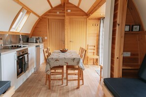 Une cuisine chaleureuse, aménagée dans le style d’un chalet en bois, avec un coin repas comprenant une grande table, des chaises et un four encastré.