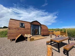A wooden cabin with a large window and a door, a wooden bench, and a picnic table. - Coastal Family Cabin with Wood Fired Hot Tub (Cockburnspath)