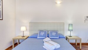 A neatly made bed with a blue bedspread and matching pillows, two bedside tables with lamps, and a clean, simple room layout.