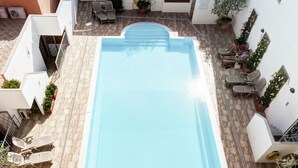 A rooftop swimming pool with a tiled deck, lounge chairs, and potted plants.