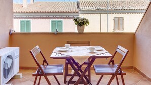 A small outdoor dining area with a table and four chairs, a potted plant, and a white air conditioning unit.