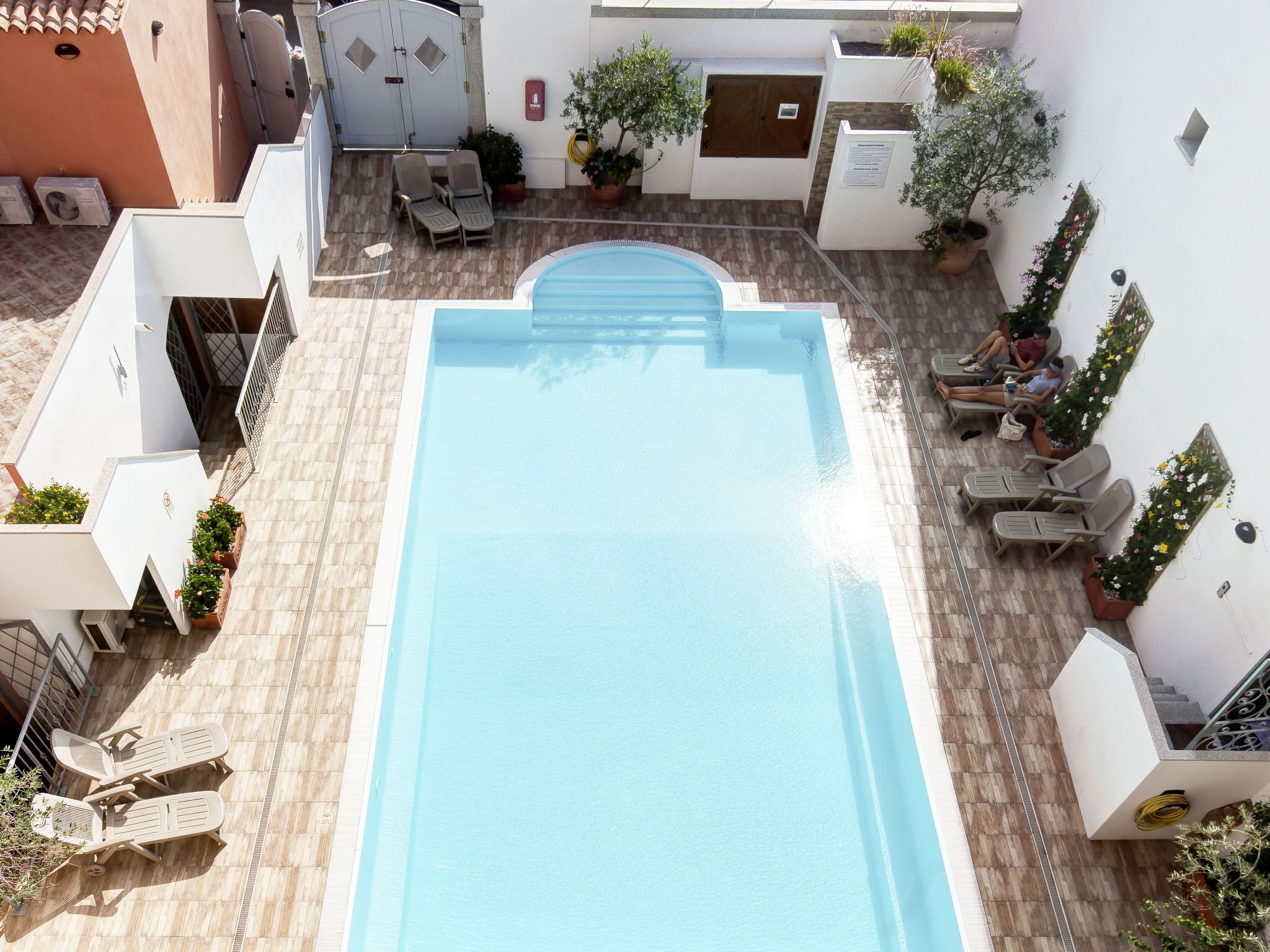 A rooftop swimming pool with a tiled deck, lounge chairs, and potted plants.
