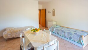 Una habitación pequeña y limpia con una cama, una mesa con un frutero y un aparador.