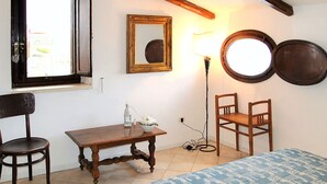 A room with a wooden table, two chairs, a bed with a patterned bedspread, a mirror, a lamp, and a window with a view of the outside. - Casa Belvedere by Interhome (Gaeta)