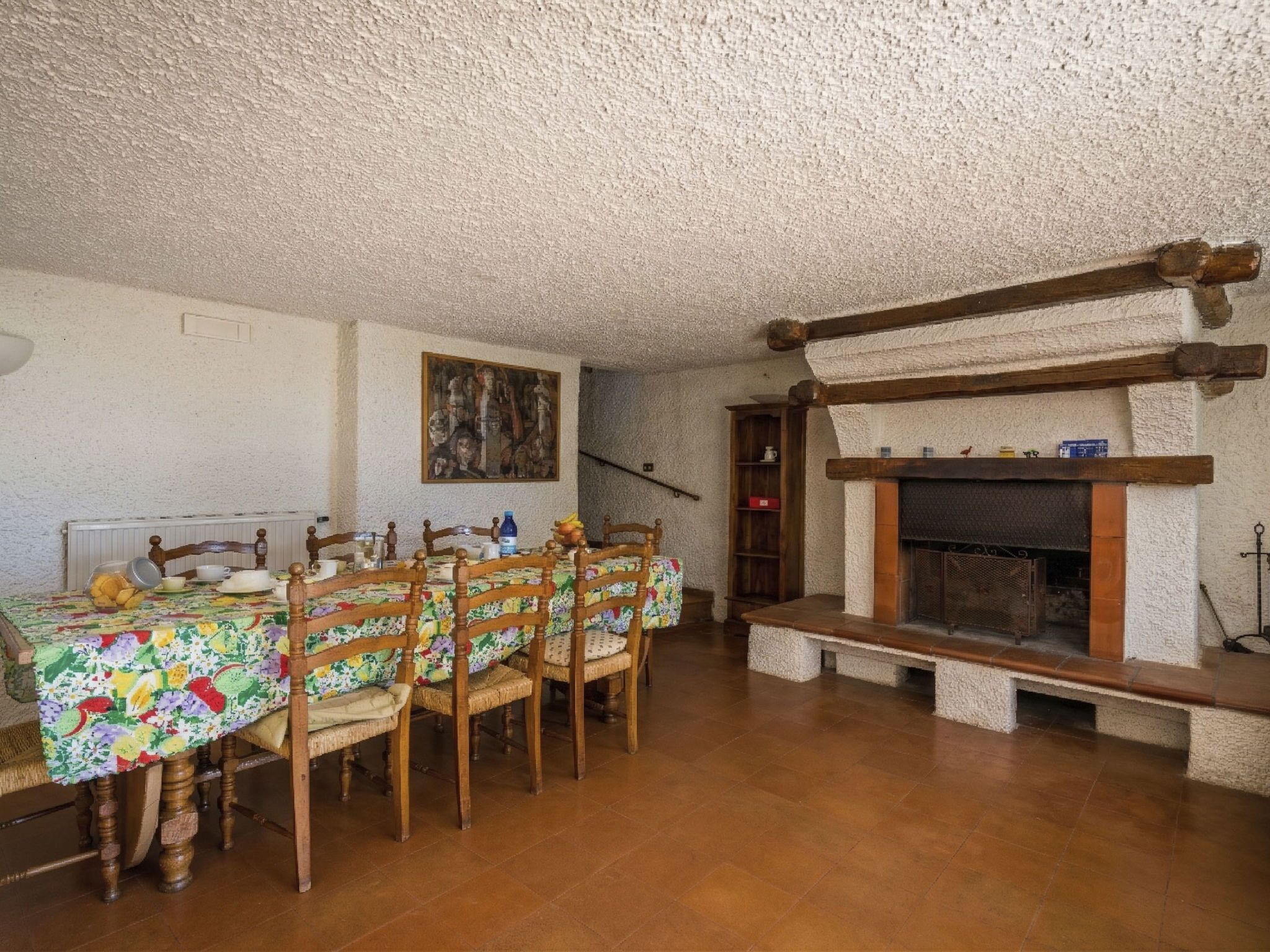 Un comedor con una mesa dispuesta para seis personas, sillas de madera, una chimenea y un cuadro en la pared.