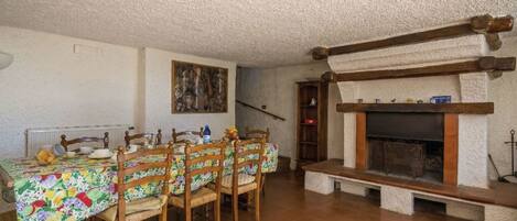 Un comedor con una mesa dispuesta para seis personas, sillas de madera, una chimenea y un cuadro en la pared.