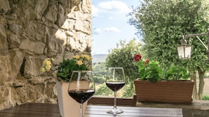 Un muro de piedra, dos macetas con flores y dos copas de vino sobre una mesa de madera.
