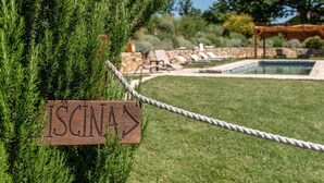 Un letrero de madera indica 'ISCINA' señalando a la derecha, un área de piscina con sillones de descanso y una barrera de cuerda.