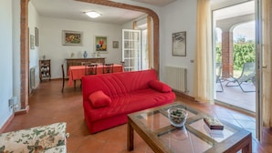 A living room with a red sofa, a glass coffee table, and a dining area with a red tablecloth.