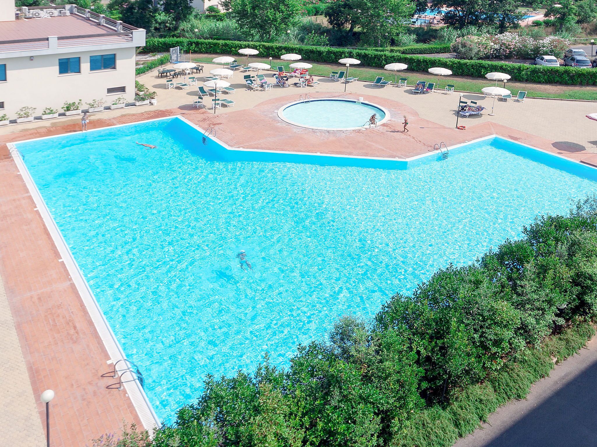 Una piscina rectangular grande con un jacuzzi circular, rodeada de sillones y sombrillas.