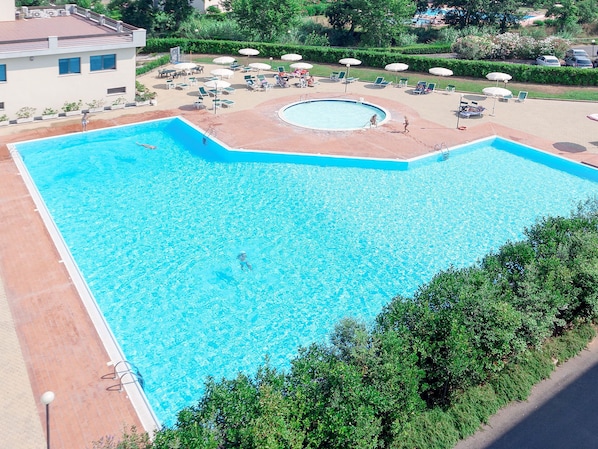 A large rectangular swimming pool with a circular hot tub, surrounded by lounge chairs and umbrellas.