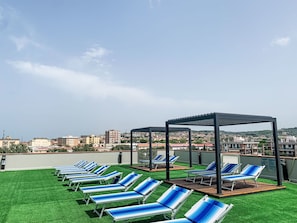 A rooftop terrace with multiple lounge chairs and a pergola structure.