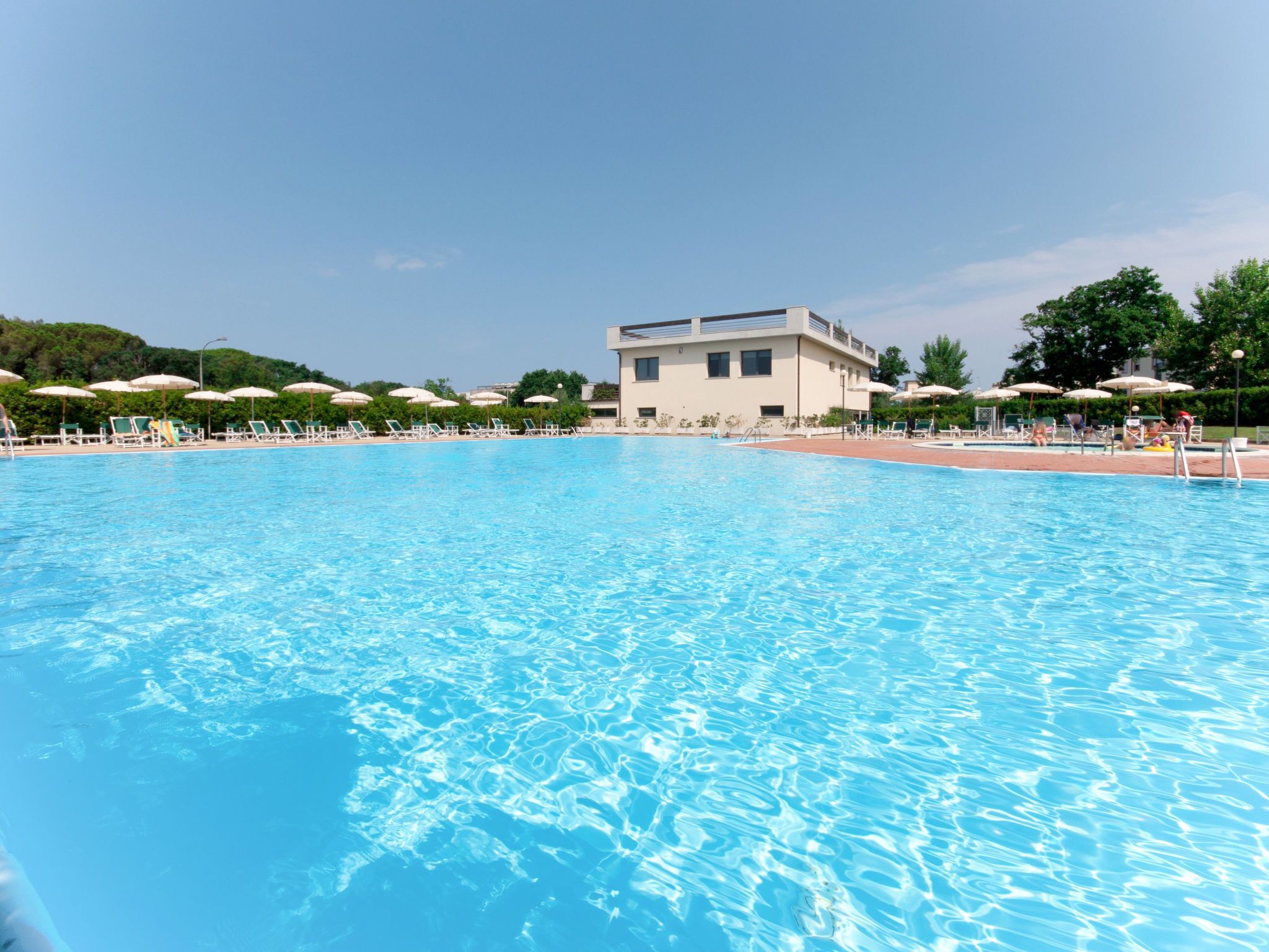 A swimming pool with lounge chairs and umbrellas, surrounded by a building with a flat roof.