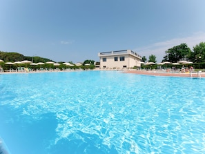 A swimming pool with lounge chairs and umbrellas, surrounded by a building with a flat roof. - Santa Costanza by Interhome (San Vincenzo)