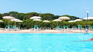 Une piscine entourée de verdure, avec des chaises longues et des parasols.