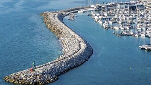 Un port de plaisance avec des bateaux amarrés, une digue rocheuse et une statue sur une petite île.