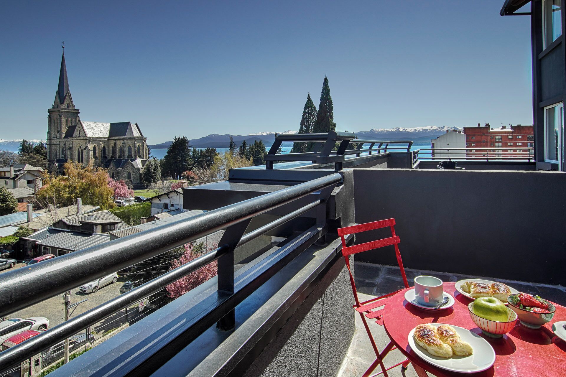 Un balcon avec une table préparée pour le petit-déjeuner, d’où l’on peut admirer une église et des montagnes.